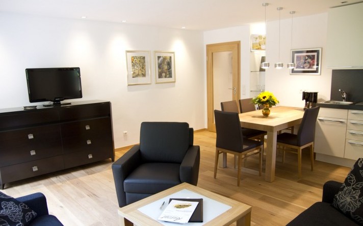 De woonkamer met kitchenette in de vakantiewoning “Auf der Tenne” in het Schneisberghaus van Hotel Jagdhaus Wiese in het Sauerland is licht en modern ingericht.